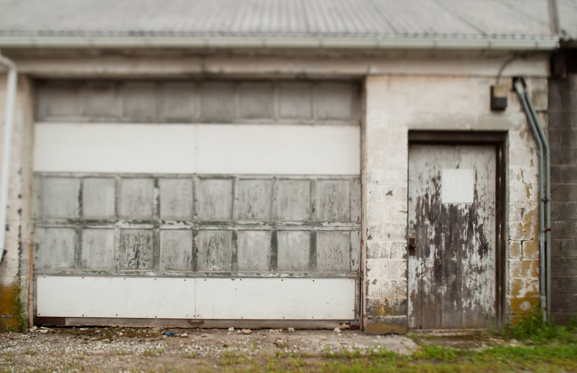 Weathered detached block garage with the roll-up door closed, before removal